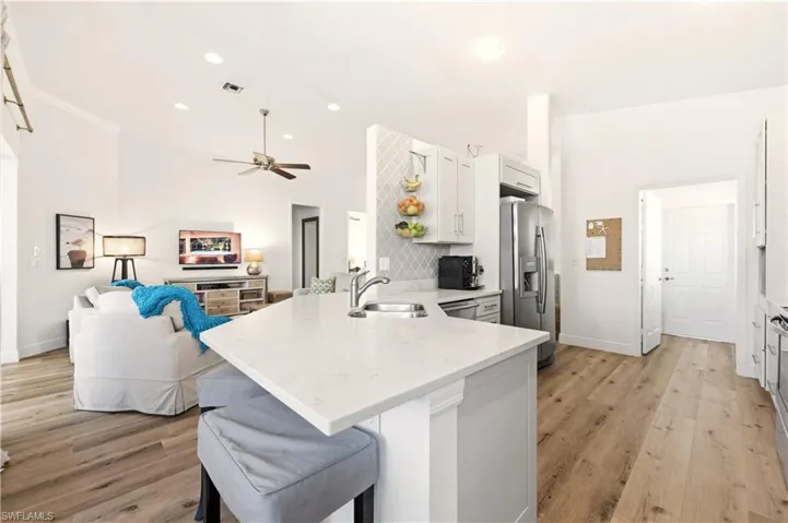 Kitchen with a kitchen bar, a peninsula, Luxury Vinyl flooring, stainless steel fridge with ice dispenser, and white cabinetry