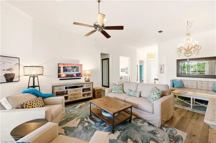 Great room with crown molding, with Luxury Vinyl floors, a chandelier, and ceiling fan