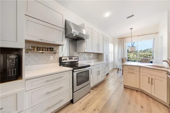 Kitchen with electric range, exhaust hood, black microwave, Luxury Vinyl floors, and decorative light fixtures