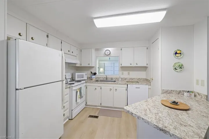 countertops, white cabinets, light wood finished floors, and a peninsula