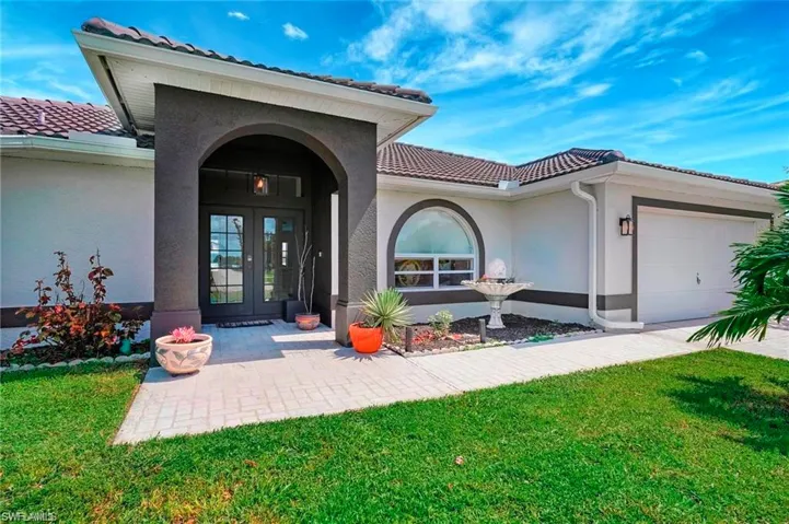 Entrance to property with french doors, stucco siding, a lawn, a tile roof, and an attached garage