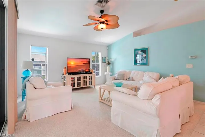 Living area with ceiling fan, plenty of natural light, and light colored carpet