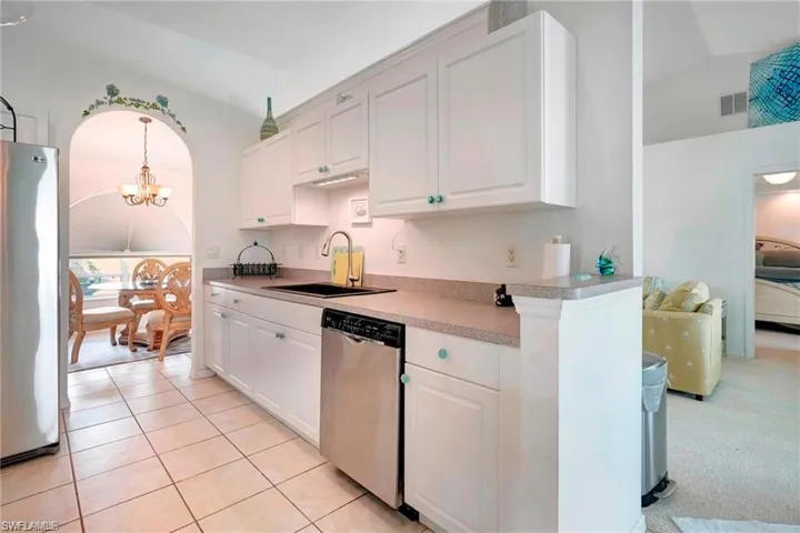 Kitchen featuring stainless steel appliances, white cabinets, hanging lights, arched walkways, and light countertops