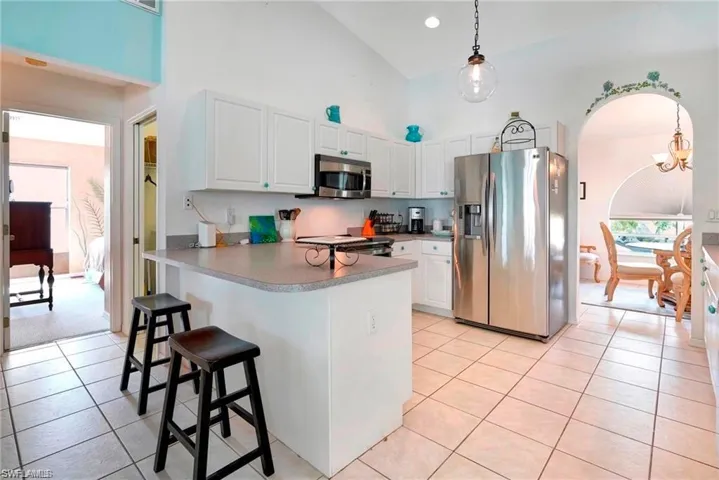 Kitchen featuring stainless steel appliances, arched walkways, a peninsula, white cabinets, and hanging light fixtures