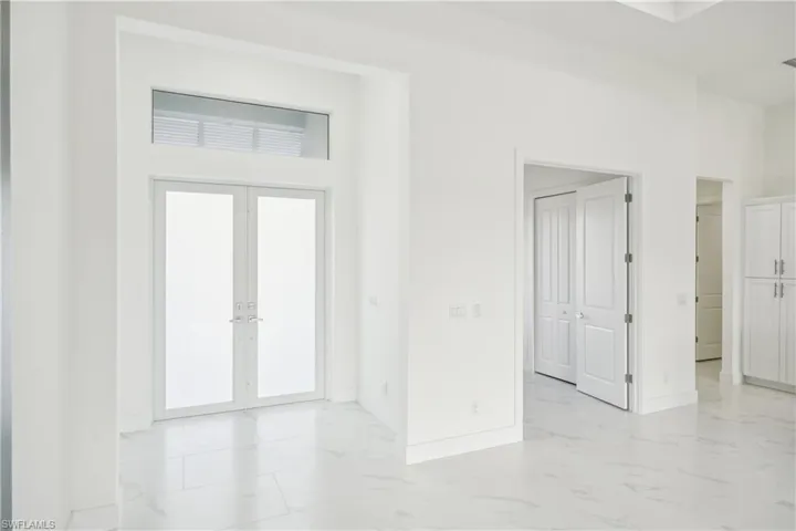 Unfurnished room featuring french doors, baseboards, marble finish floor, a towering ceiling, and visible vents