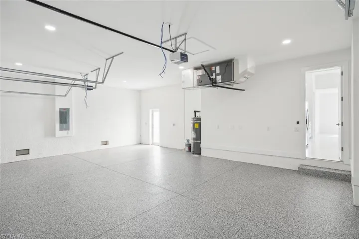 Garage featuring electric panel, recessed lighting, a garage door opener, and secured water heater