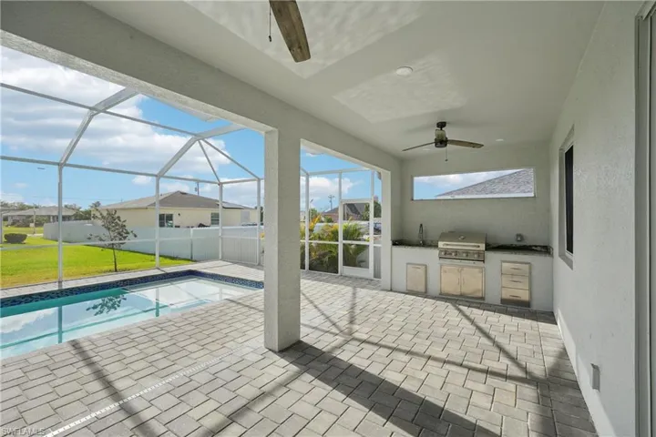 Pool featuring a patio, glass enclosure, a ceiling fan, area for grilling, and an outdoor kitchen