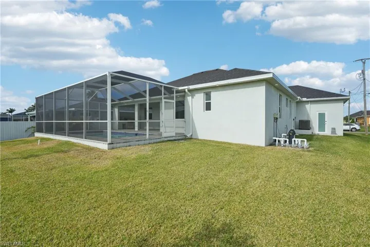 Rear view of house with an outdoor pool, stucco siding, a lanai, and a yard