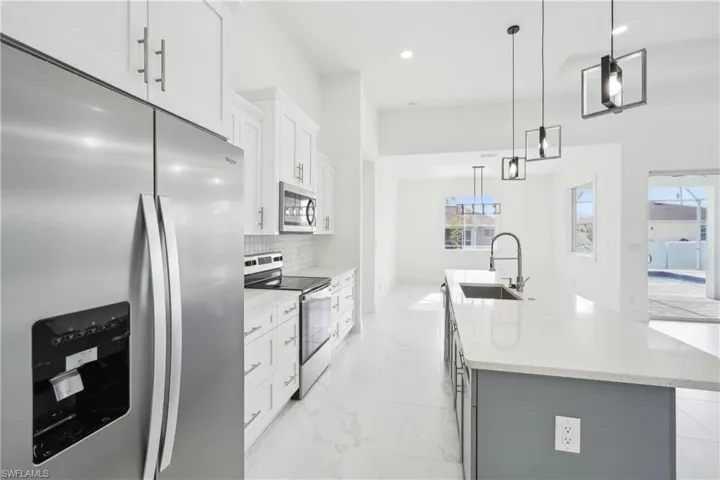 Kitchen with marble finish floor, a kitchen island with sink, stainless steel appliances, a sink, and backsplash