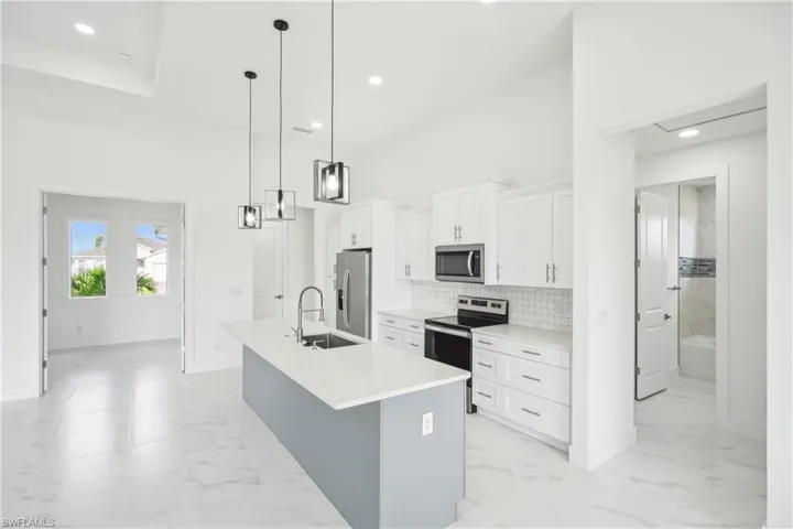Kitchen featuring marble finish floor, stainless steel appliances, a center island with sink, a sink, and backsplash
