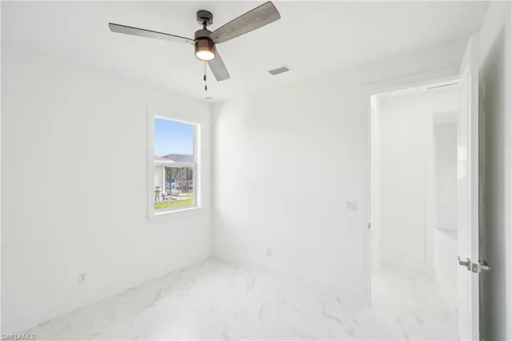 Empty room with marble finish floor, baseboards, visible vents, and a ceiling fan