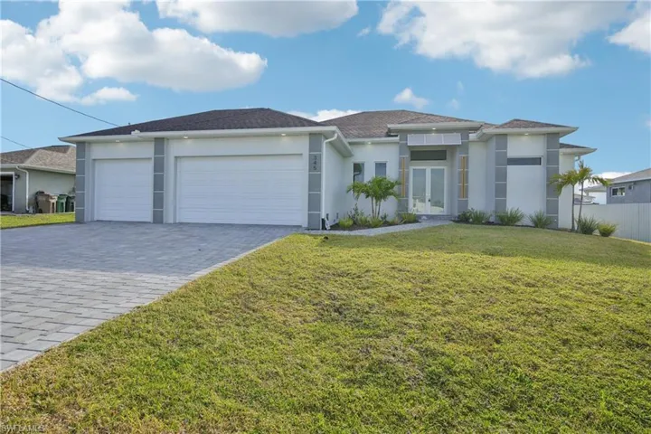View of front of property with a front yard, french doors, stucco siding, an attached garage, and decorative driveway