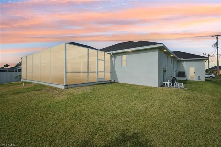 Back of property at dusk featuring glass enclosure, stucco siding, fence, and a yard