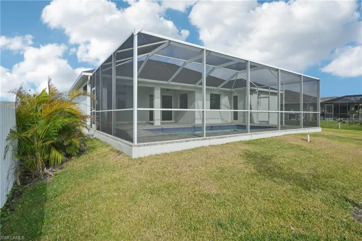 Rear view of property with a lawn, glass enclosure, a patio area, and an outdoor pool