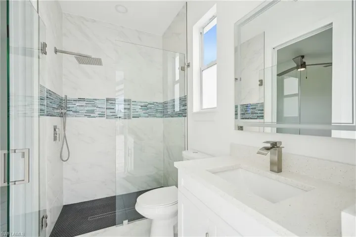 Full bathroom featuring a ceiling fan, toilet, vanity, and a stall shower
