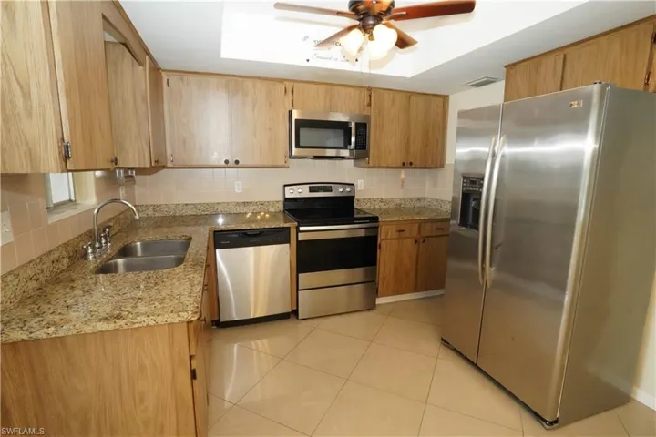 Kitchen featuring stainless steel appliances, light stone counters, tasteful backsplash, light tile patterned floors, and a ceiling fan