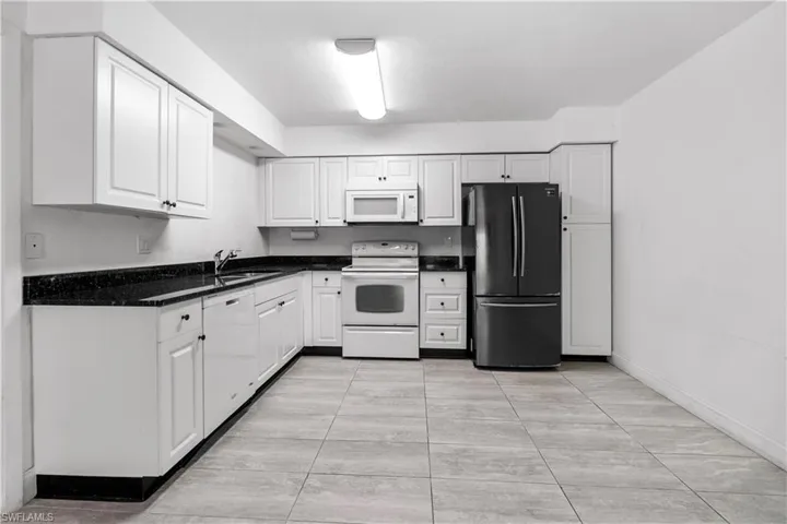 Kitchen with white appliances, white cabinets, dark stone counters, and light tile patterned floors