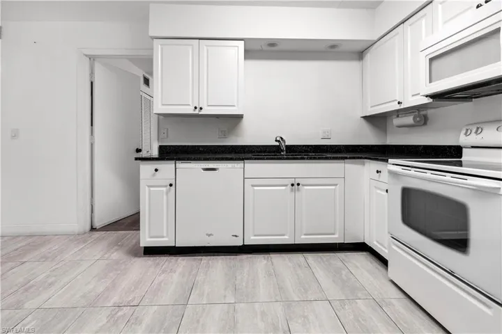 Kitchen with white appliances, white cabinets, and dark stone counters