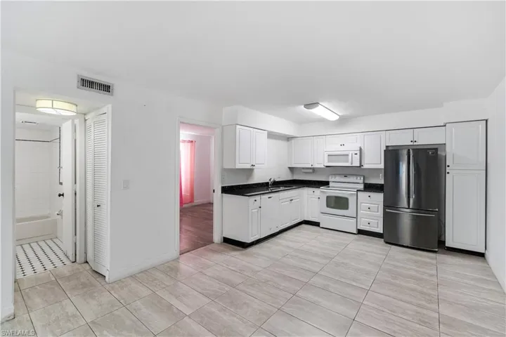 Kitchen with white appliances, white cabinetry, dark countertops, and light tile patterned floors