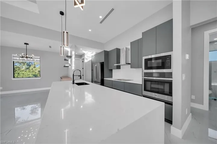 Kitchen featuring an island with sink, modern cabinets, appliances with stainless steel finishes, wall chimney exhaust hood, and gray cabinets