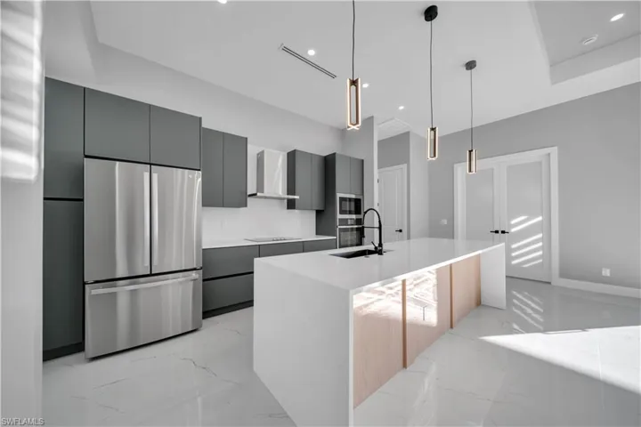 Kitchen featuring stainless steel appliances, light marble finish floors, an island with sink, decorative light fixtures, and recessed lighting