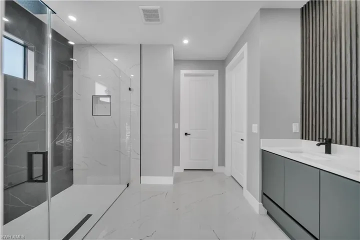 Bathroom with vanity, a marble finish shower, recessed lighting, and light marble finish flooring