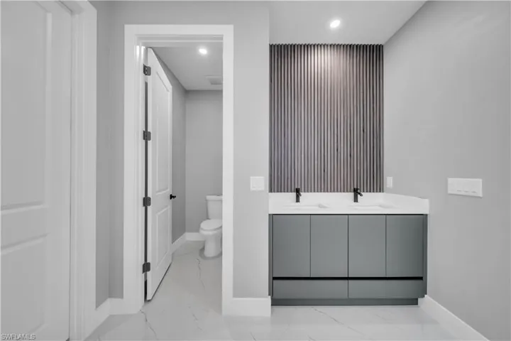 Full bath with recessed lighting, double vanity, and light marble finish floors