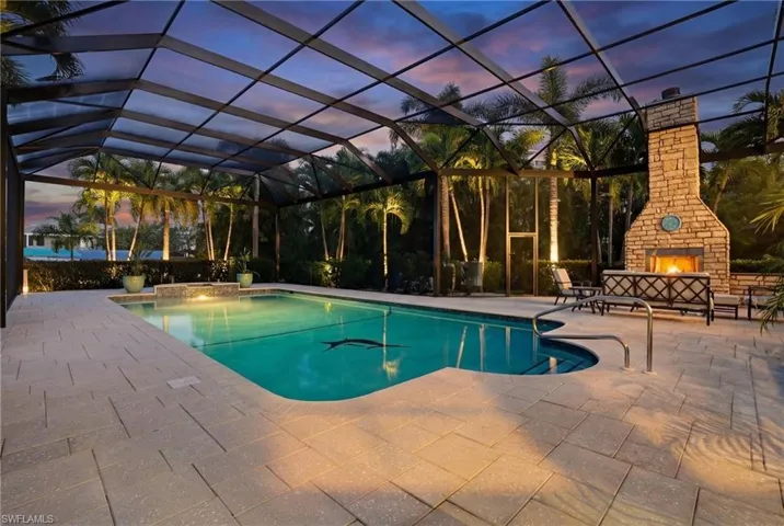 Outdoor pool with glass enclosure, an outdoor stone fireplace, a patio, and a sunroom