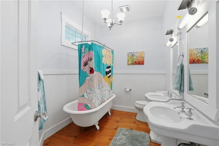 Full bath featuring a wainscoted wall, hardwood / wood-style flooring, a chandelier, and a combined bath / shower with freestanding tub