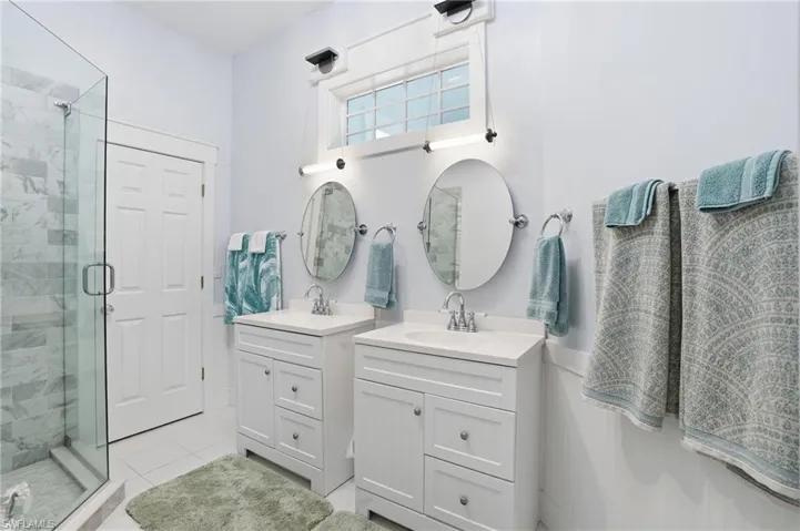 Bathroom with two vanities, a shower stall, and light tile patterned floors