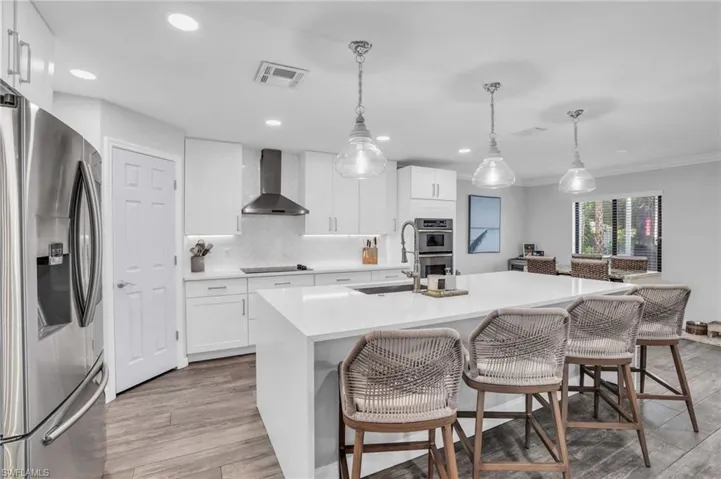 Kitchen featuring sink, appliances with stainless steel finishes, wall chimney exhaust hood,  and a center island with waterfall quartz countertops