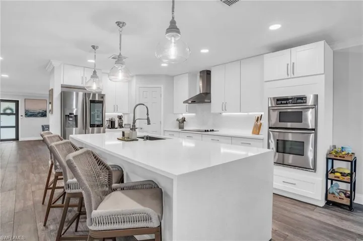 Kitchen featuring tile backsplash, sink, appliances with stainless steel finishes, double wall oven and coastal pendant lighting