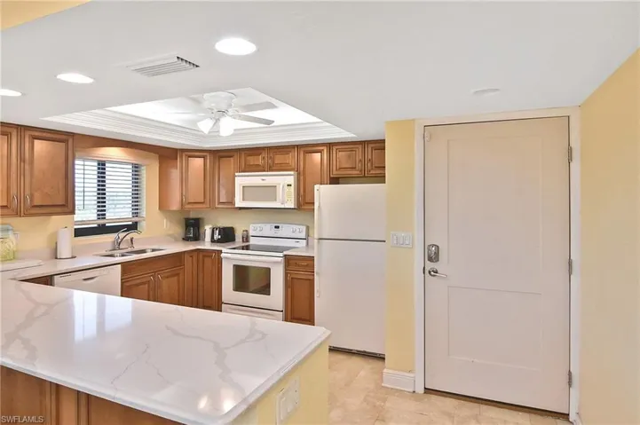Kitchen featuring a raised ceiling, recessed lighting, white appliances, brown cabinets, and a peninsula