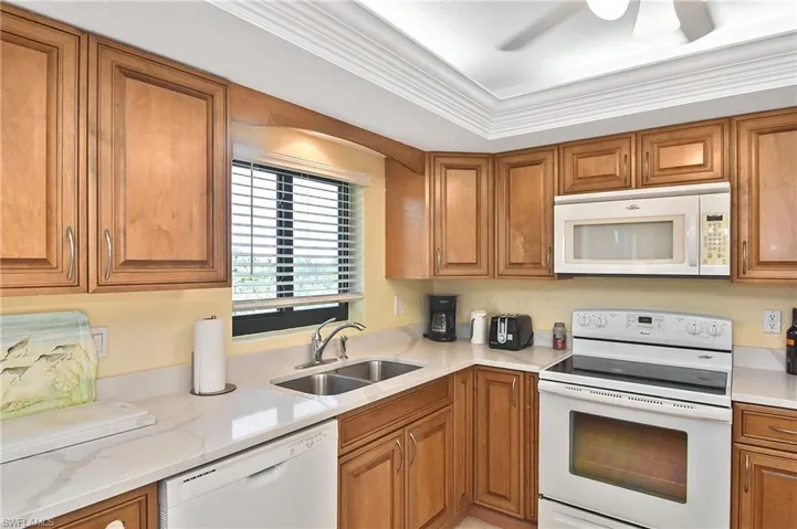 Kitchen featuring white appliances, brown cabinetry, and ornamental molding