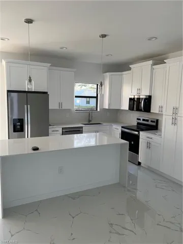 Kitchen with hanging light fixtures, stove, white cabinets, a sink, and fridge