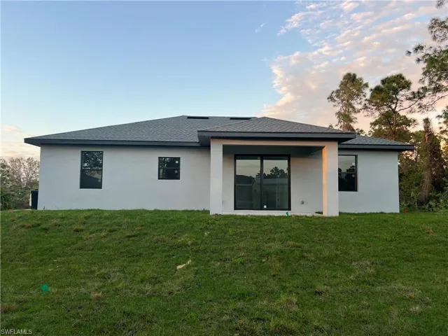 Back of property featuring a yard, a shingled roof, and stucco siding