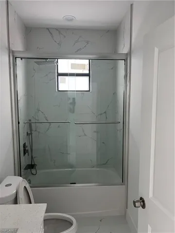 Bathroom featuring marble finish floor, enclosed tub / shower combo, vanity, and toilet