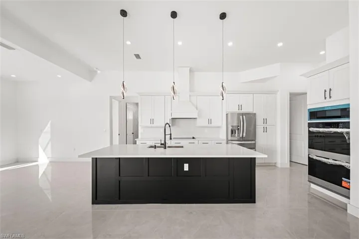 Spacious kitchen featuring a large black island with a white countertop, white cabinetry, integrated stainless steel appliances, and ceiling-mounted pendant lighting