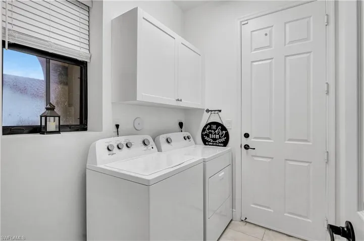 Clothes washing area featuring cabinets, light tile patterned floors, and washer and clothes dryer