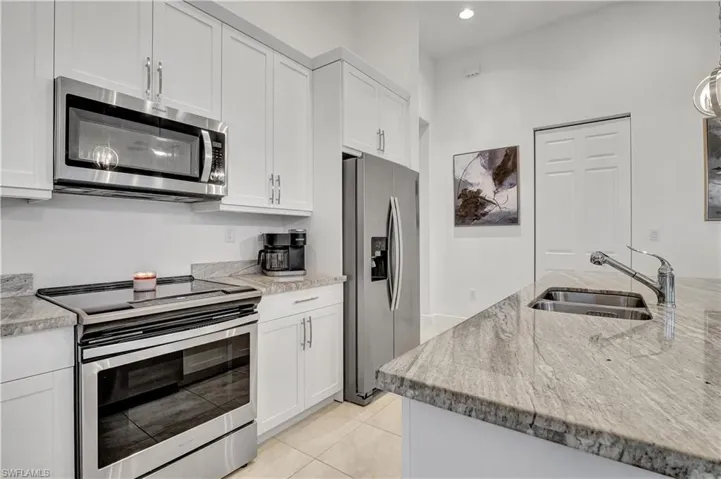 Kitchen featuring white cabinets, light stone countertops, light tile patterned floors, stainless steel appliances, and sink