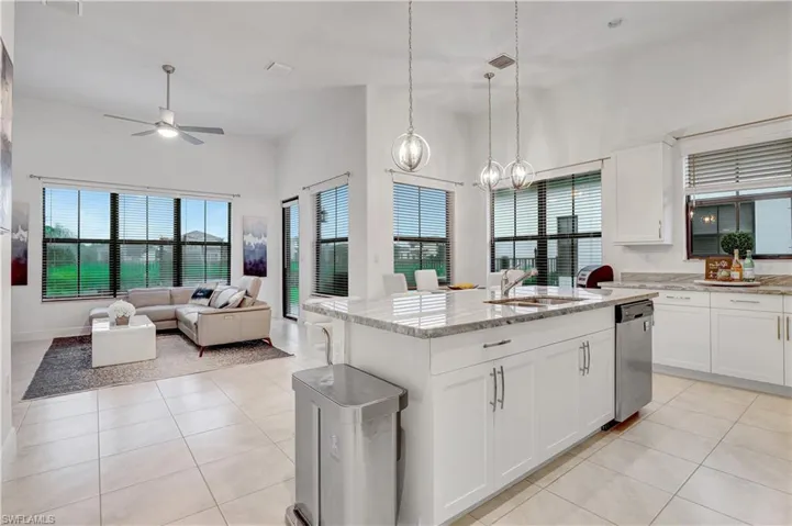Kitchen featuring white cabinets, an island with sink, ceiling fan with notable chandelier, and dishwasher