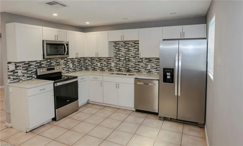Kitchen featuring white cabinetry, light-toned countertops, stainless steel appliances, a tile backsplash, and tile flooring