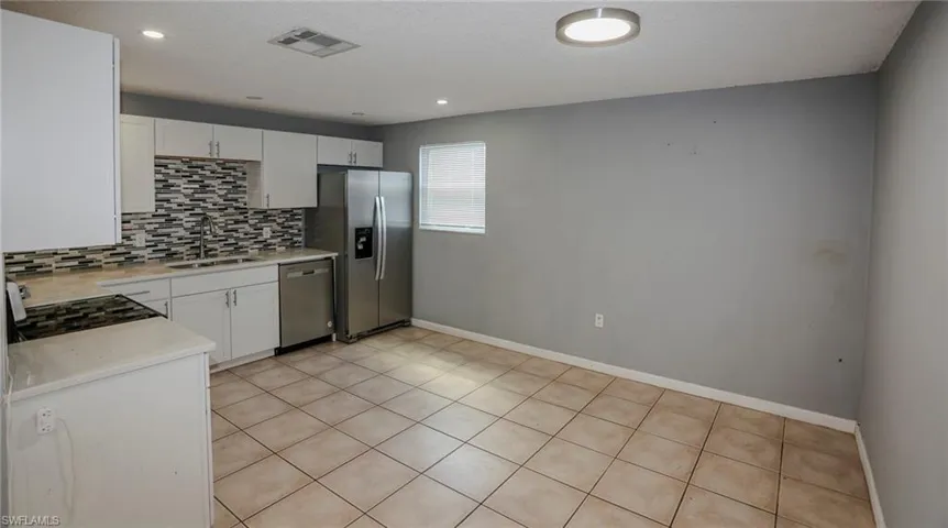 White cabinetry with stainless steel appliances, mosaic tile backsplash, and light-toned tile flooring