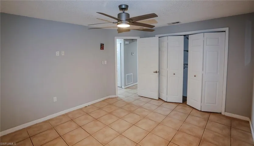 Neutral wall paint, ceiling-mounted fan with integrated lighting, ceramic tile flooring, and bi-fold closet doors