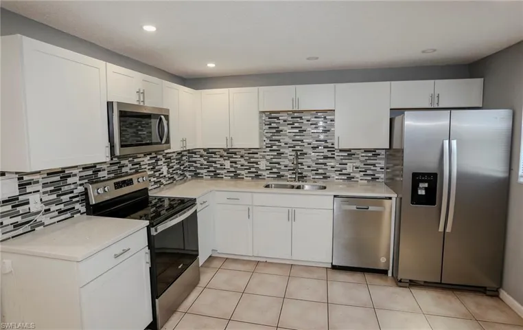 Contemporary kitchen with white cabinetry, stainless steel appliances, mosaic tile backsplash, and light-toned countertops