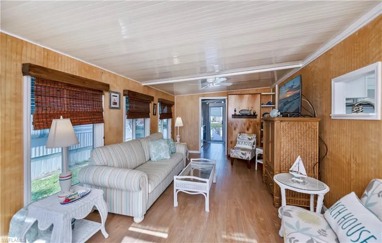 Living area with wood finished floors, wooden walls, a ceiling fan, and crown molding