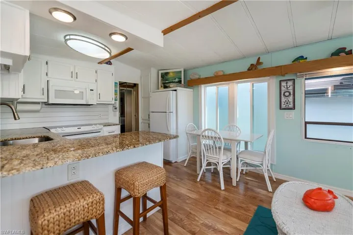 Kitchen featuring white appliances, white cabinets, a peninsula, a breakfast bar area, and light wood-style floors