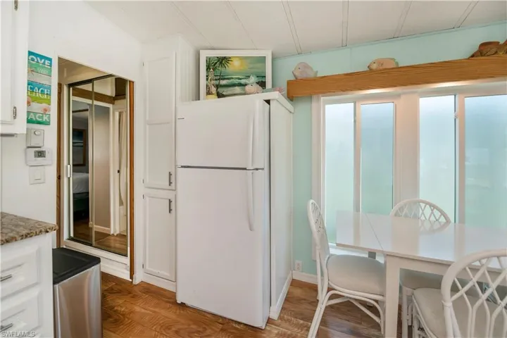Kitchen with freestanding refrigerator, white cabinetry, light wood-style floors, and stone countertops