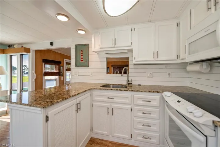 Kitchen with white appliances, a peninsula, white cabinetry, dark stone countertops, and wood walls