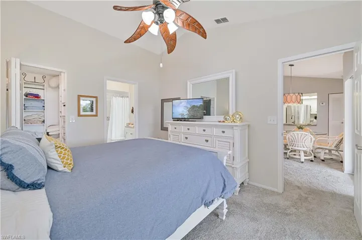 Bedroom with light colored carpet, ensuite bath, visible vents, ceiling fan, and a walk in closet